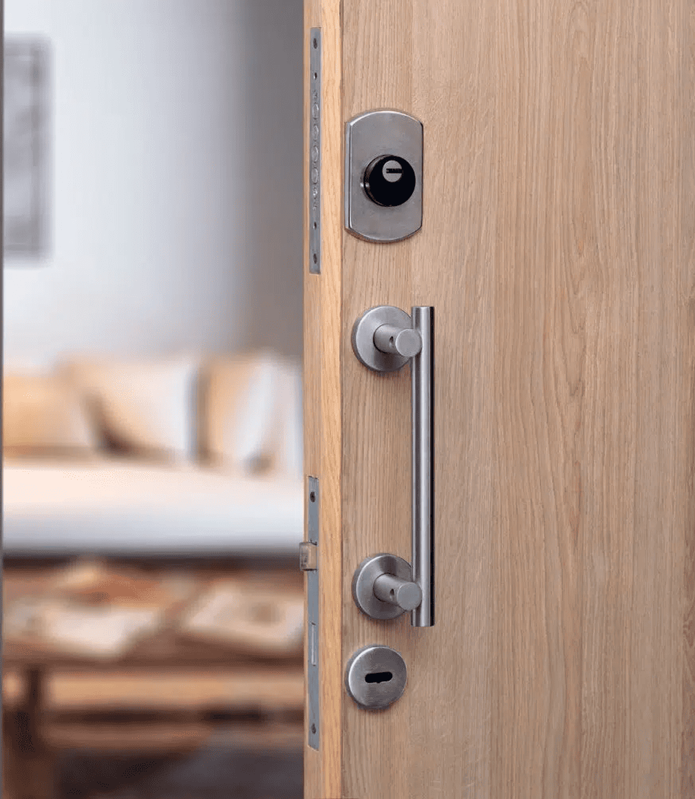 Eine Holztür ist leicht geöffnet und zeigt einen modernen silbernen Türgriff, zwei Schlösser und ein intelligentes Schloss. Im unscharfen Hintergrund ist ein Wohnzimmer mit einem Sofa und einem Tisch zu sehen.