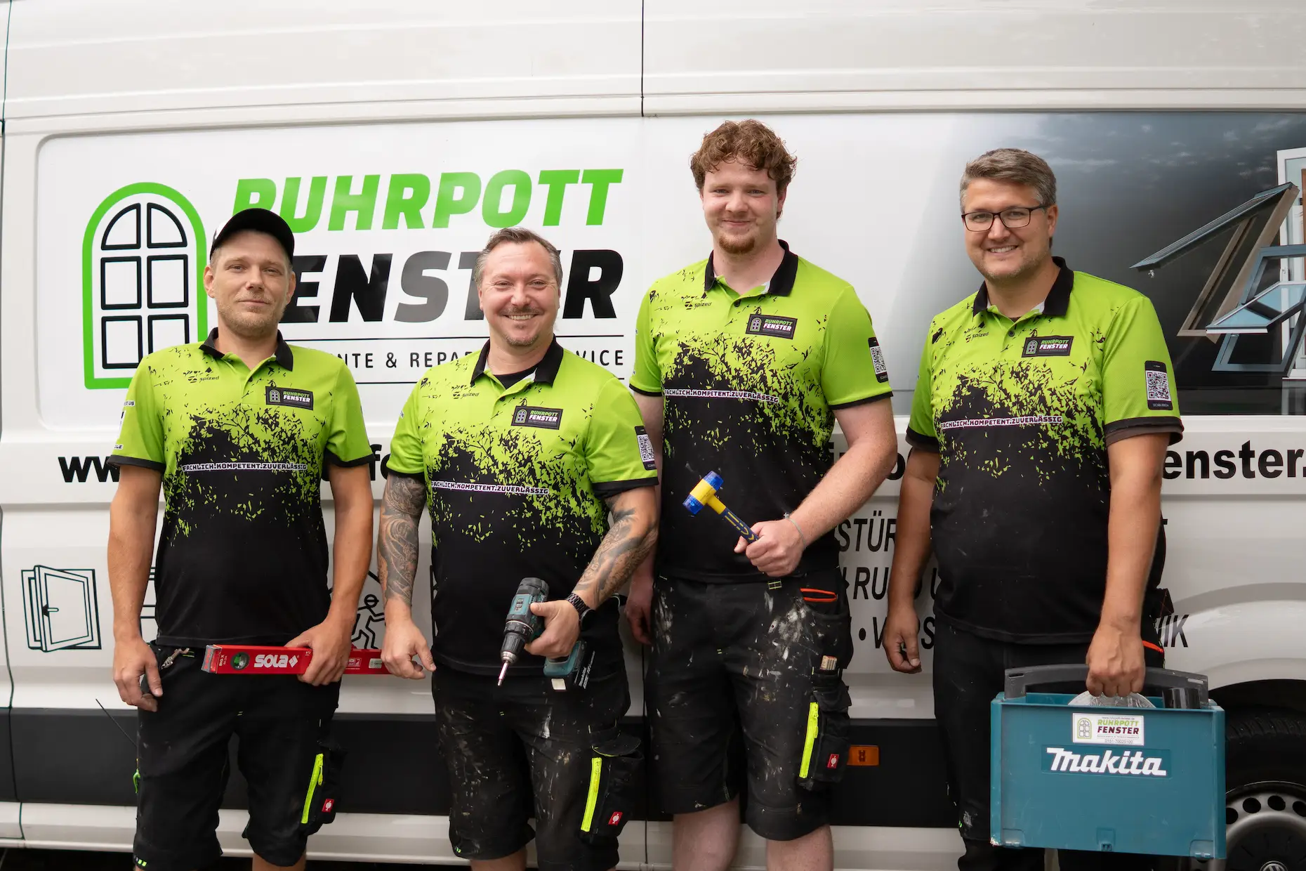 Vier Männer in grün-schwarzen Arbeitsuniformen stehen lächelnd vor einem Lieferwagen mit der Aufschrift "Ruhrpott Fenster". Jeder von ihnen hält Werkzeug in der Hand, was darauf hindeutet, dass sie zu einem Fensterreparatur- oder -montageteam gehören.